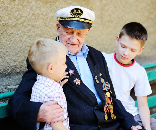 WWII veteran with children. Grandchildren looking at grandfather's military awards.
